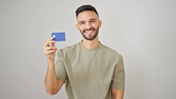 孤立した白い背景の上にクレジットカードを持っている自信を持って微笑む若いヒスパニックの男 - 写真・画像