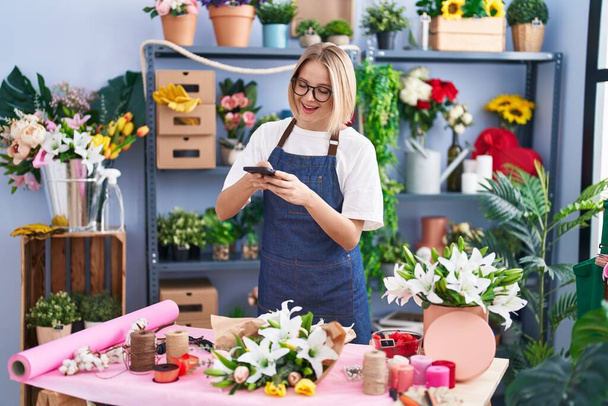 Young blonde woman florist make photo by smartphone to flowers at florist shop - Photo, Image