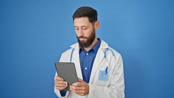 Молодой латиноамериканец врач с помощью тачпада на изолированном синем фоне - Фото, изображение