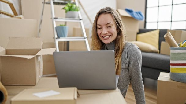 Young caucasian woman using laptop sitting on floor at new home - Photo, Image