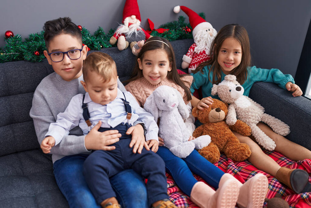 自宅でクリスマスの装飾でソファーに座って自信を持って微笑む子供のグループ - 写真・画像