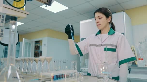Gericht Wetenschapper inspecteren reageerbuis met blauwe chemische vloeistof. Donkerharige vrouw in het lab Uniform en handschoenen voeren laboratoriumanalyse uit. Biochemie Concept. - Video