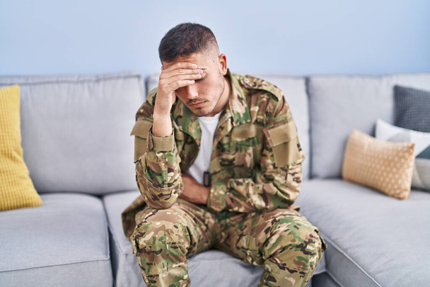 Young hispanic man army soldier sitting on sofa stressed at home - Photo, Image
