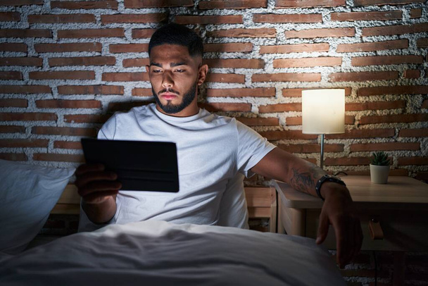 Jovem latino usando touchpad sentado na cama no quarto - Foto, Imagem
