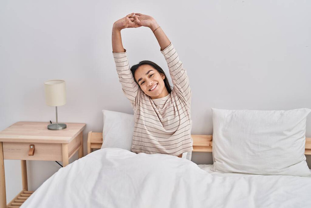 Young hispanic woman waking up stretching arms at bedroom - Photo, Image
