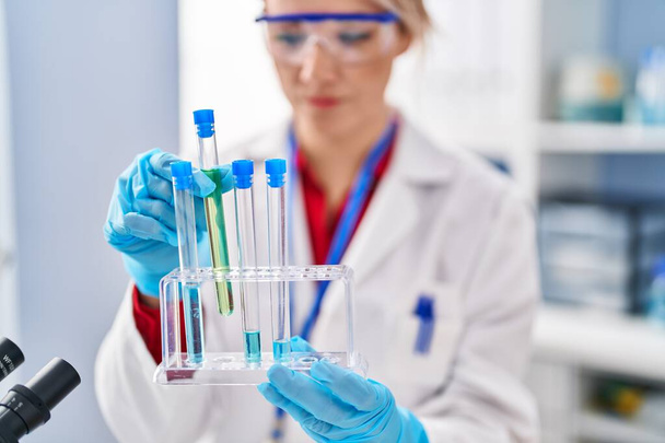 Joven mujer rubia científica sosteniendo tubos de ensayo en laboratorio - Foto, imagen