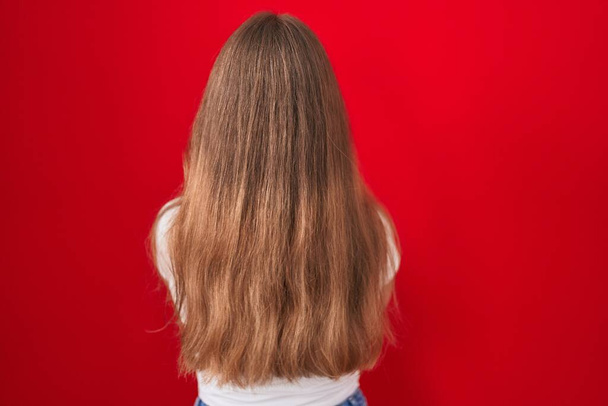Young caucasian woman standing over red background standing backwards looking away with crossed arms  - Photo, Image