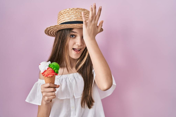 Chica adolescente sosteniendo helado sorprendido con la mano en la cabeza por error, recordar el error. olvidado, mal concepto de memoria.  - Foto, Imagen