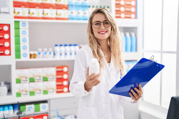 Nuori nainen apteekissa lukeminen raportti tilalla pillereitä pullo apteekissa - Valokuva, kuva