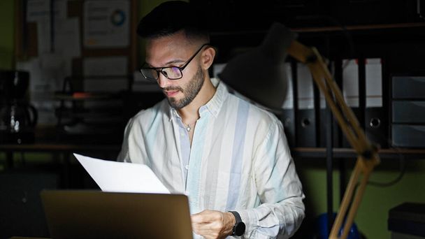 Jeune homme hispanique travailleur d'affaires en utilisant un document de lecture d'ordinateur portable au bureau - Photo, image