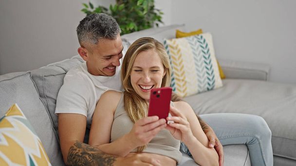 Man and woman couple using smartphone sitting on sofa at home - Fotografie, Obrázek