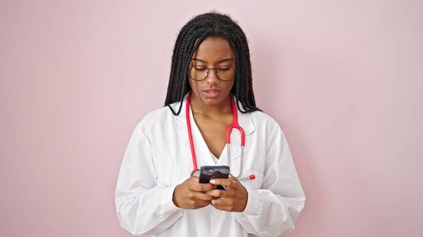 Afroamerykanka lekarz uśmiecha się za pomocą smartfona na odizolowanym różowym tle - Zdjęcie, obraz