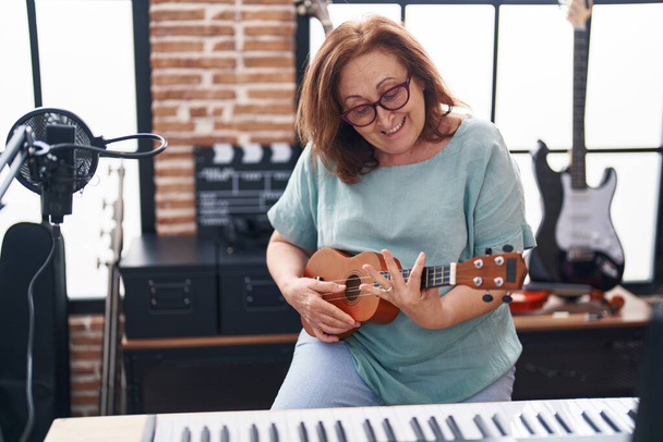 Senior femme musicien souriant confiant jouer ukulele au studio de musique - Photo, image