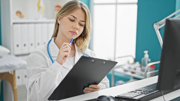 Młoda blondynka lekarz czyta na tablicy myśląc w klinice - Zdjęcie, obraz