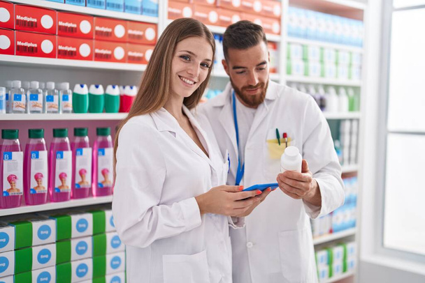 Άνδρας και γυναίκα φαρμακοποιοί που χρησιμοποιούν touchpad κρατώντας χάπια μπουκάλι στο φαρμακείο - Φωτογραφία, εικόνα