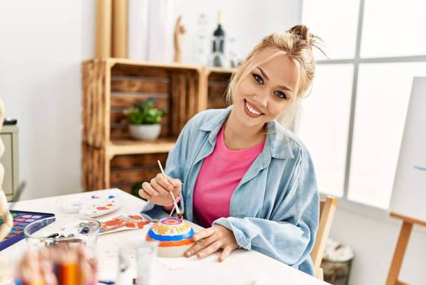 Beyaz kadın sanatçı, resim stüdyosunda kendine güvenen bir şekilde gülümsüyor. - Fotoğraf, Görsel