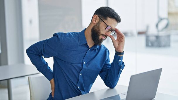 Giovane uomo ispanico lavoratore d'affari prendendo gli occhiali fuori sofferenza per mal di schiena in ufficio - Foto, immagini