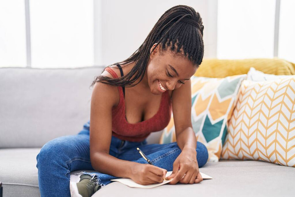 Afrikkalainen amerikkalainen nainen kirjoittaa kannettavan istuu sohvalla kotona - Valokuva, kuva