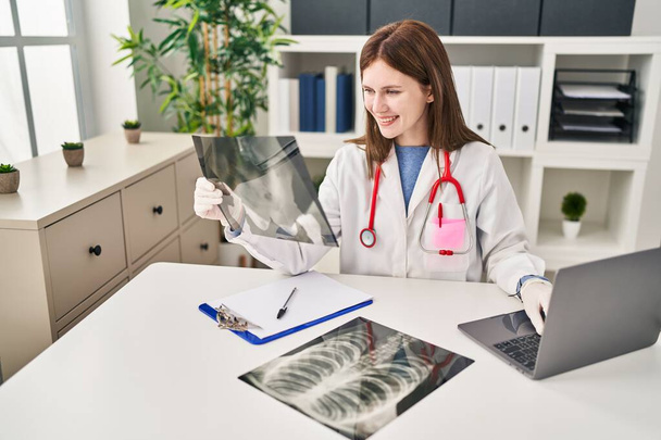 Mujer rubia joven médico buscando rayos X sentado en la mesa en la clínica - Foto, imagen