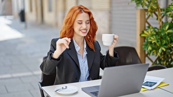 Jeune rousse femme d'affaires utilisant un ordinateur portable boire du café dansant sur la terrasse du café - Photo, image