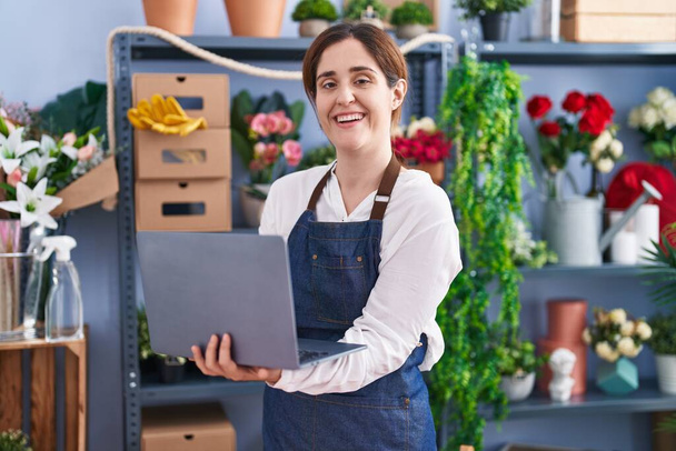 Joven florista sonriendo confiada usando laptop en floristería - Foto, Imagen