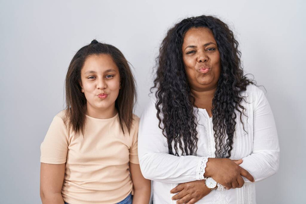Mother and young daughter standing over white background looking at the camera blowing a kiss on air being lovely and sexy. love expression.  - Photo, Image