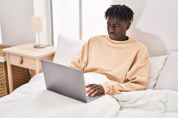 afroamericano uomo utilizzando computer portatile seduto sul letto in camera da letto - Foto, immagini
