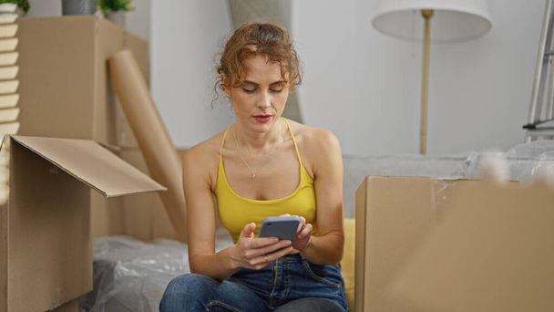 Молода жінка за допомогою смартфона сидить на дивані в новому будинку - Фото, зображення