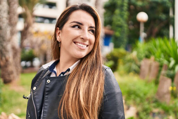 Молода красива іспаномовна жінка посміхається впевнено дивлячись в сторону в парку
 - Фото, зображення