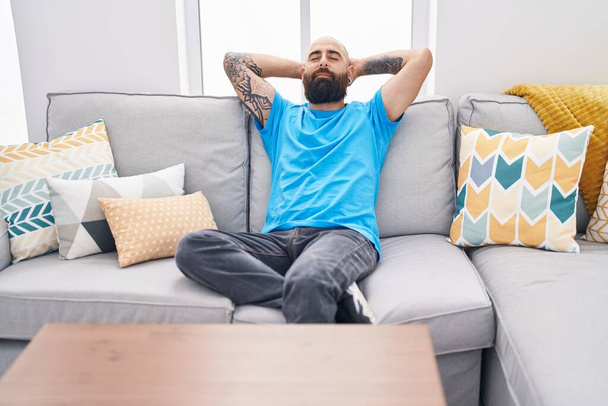 Молодий лисий чоловік розслаблений руками на голові, сидячи на дивані вдома
 - Фото, зображення