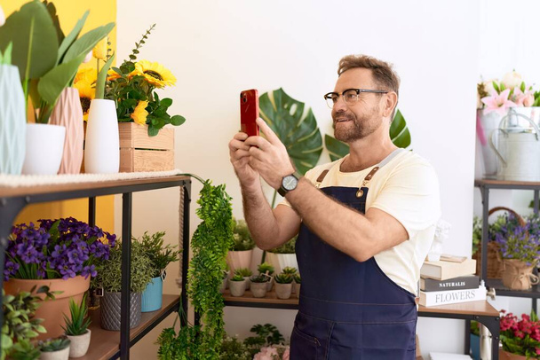 Floristería hombre de mediana edad hacer foto para florecer por teléfono inteligente en la tienda de flores - Foto, imagen