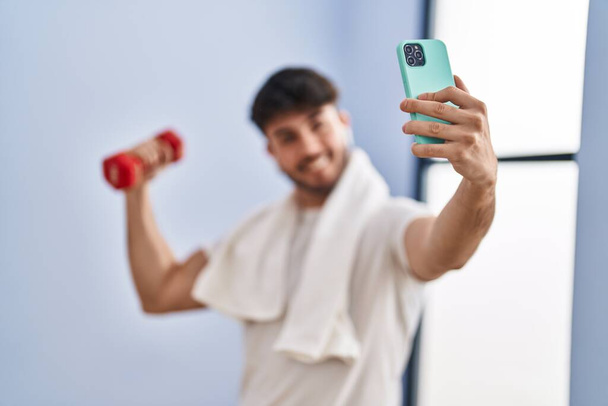 Mladý hispánec drží činku, aby selfie smartphone ve sportovním centru - Fotografie, Obrázek