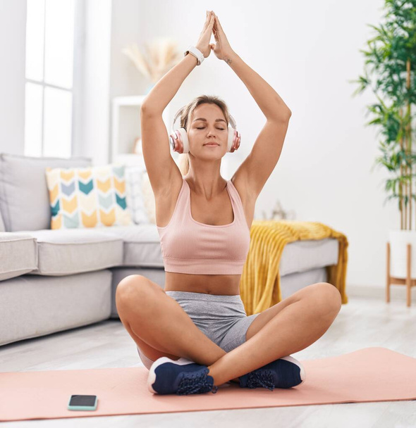 jong blond vrouw doet yoga oefening zitten op vloer thuis - Foto, afbeelding