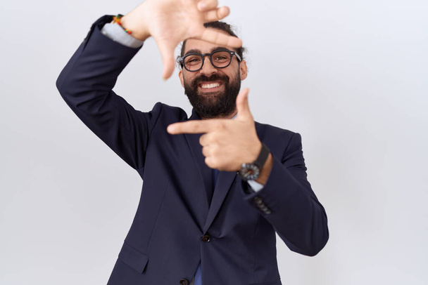 Spanyol férfi szakállas öltönyben és nyakkendőben, mosolygós képkeret kezekkel és ujjakkal, boldog arccal. kreativitás és fényképezés koncepció.  - Fotó, kép