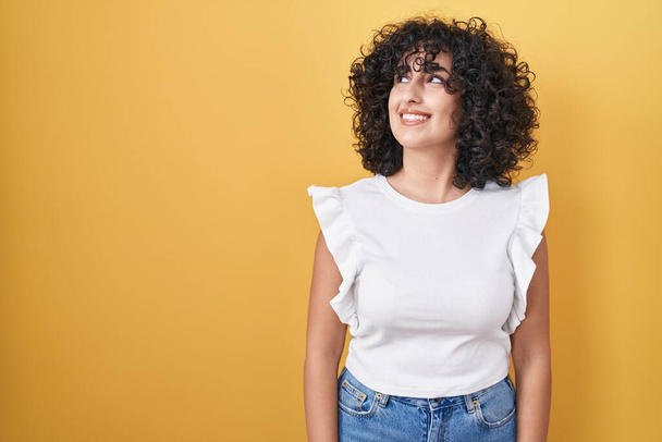 Young middle east woman standing over yellow background smiling looking to the side and staring away thinking.  - Photo, Image