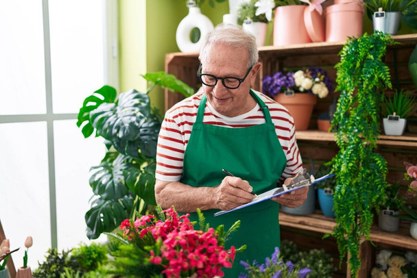 Middle age grey-haired man florist smiling confident writing on document at flower shop - Photo, Image