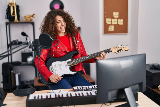 Jonge Spaanse vrouw muzikant zingen lied spelen elektrische gitaar in muziekstudio - Foto, afbeelding