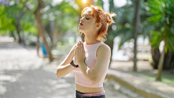 Mujer pelirroja joven con ropa deportiva entrenamiento yoga ejercicio en el parque - Foto, imagen