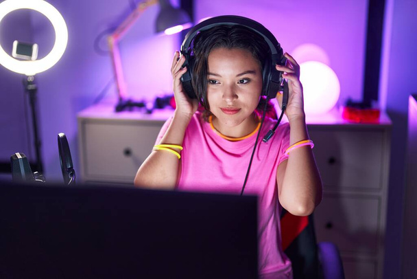 Young hispanic woman streamer smiling confident sitting on table at gaming room - Foto, afbeelding