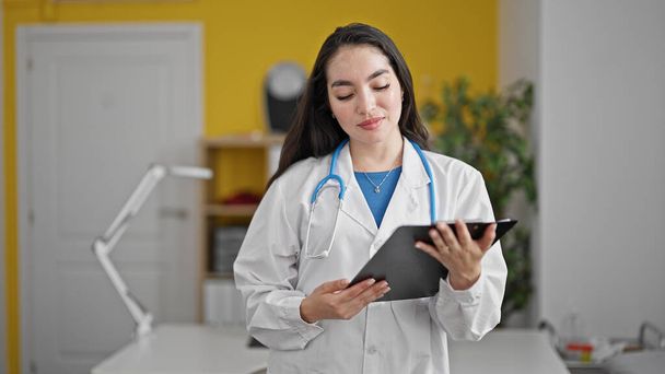 Νεαρή όμορφη Ισπανίδα γιατρός διαβάζει ιατρική έκθεση στην κλινική - Φωτογραφία, εικόνα