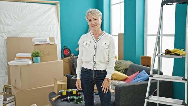Keski-ikä blondi nainen hymyilee luottavainen seisoo uudessa kodissa - Valokuva, kuva