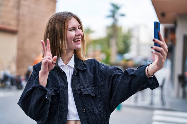 Junge blonde Frau lächelt selbstbewusst und macht Selfie mit dem Smartphone auf der Straße - Foto, Bild