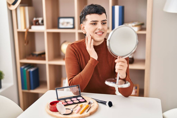 Jonge niet binaire man glimlachend zelfverzekerd kijkend op spiegel thuis - Foto, afbeelding