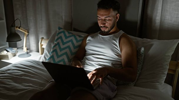 Jovem árabe homem usando laptop sentado na cama no quarto - Foto, Imagem