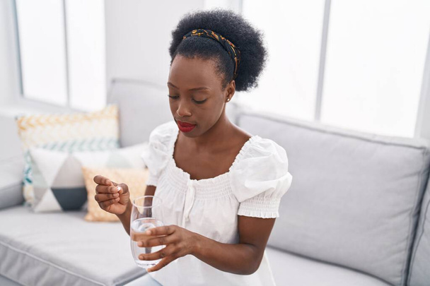 Африканская американка, принимающая таблетки сидя дома на диване - Фото, изображение
