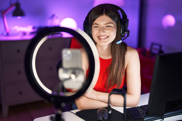 Fiatal kaukázusi nő videojáték felvétel okostelefonnal néz pozitív és boldog álló és mosolygó magabiztos mosollyal mutatja fogak  - Fotó, kép