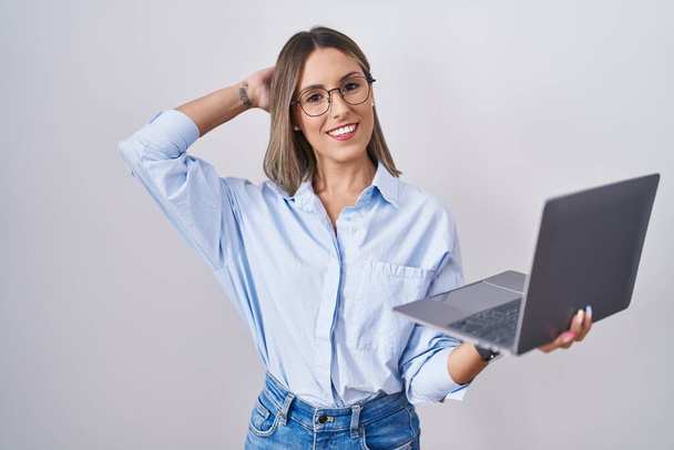 コンピュータのラップトップを使用して働く若い女性は自信を持って手のジェスチャーで髪に触れ,魅力的でファッショナブルなポーズ  - 写真・画像