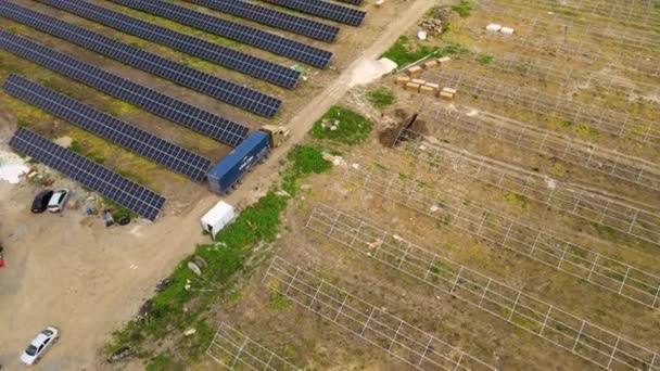 電気エネルギーの生産のための金属フレームの太陽電池パネルのためのアセンブリ部品を提供するトラックとの建設中の電力発電所の航空観察. - 映像、動画