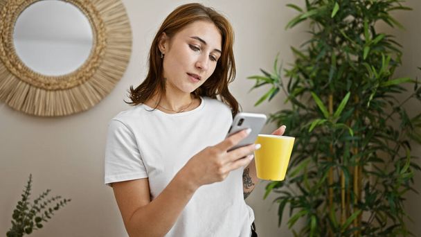 Jovem segurando xícara de café usando smartphone em casa - Foto, Imagem