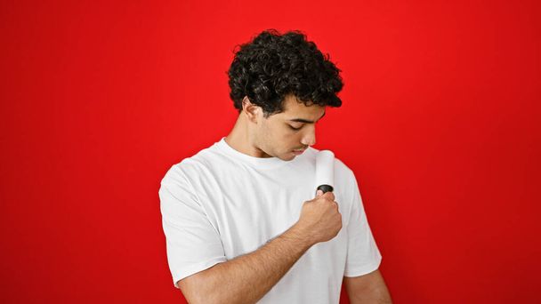 fiatal latin férfi használ stick roll tiszta kisállat haj felett elszigetelt piros háttér - Fotó, kép